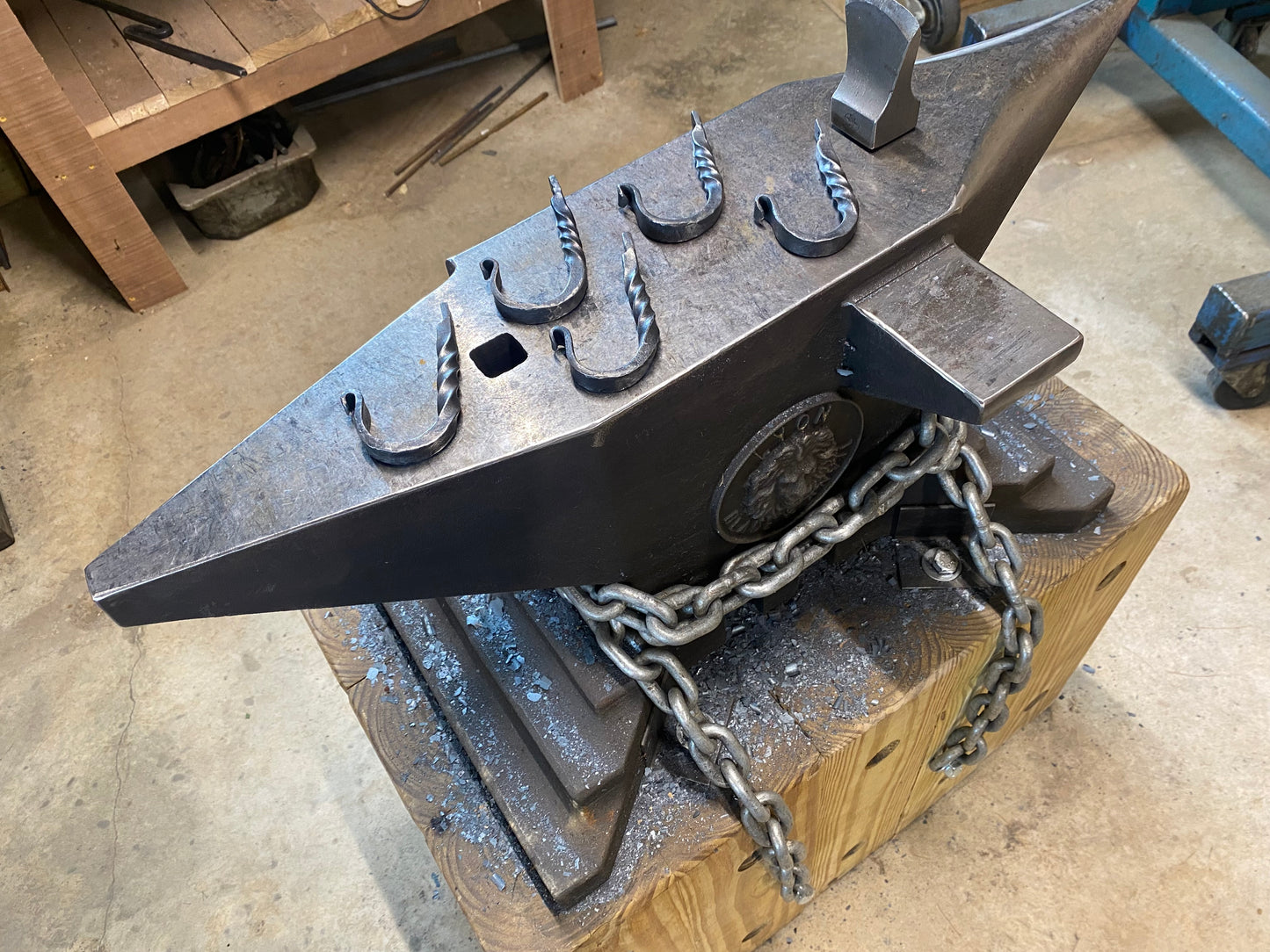 A blacksmith's anvil with six decorative, hand-forged J- hooks. The hooks are a dark metal color and have a twisted design.