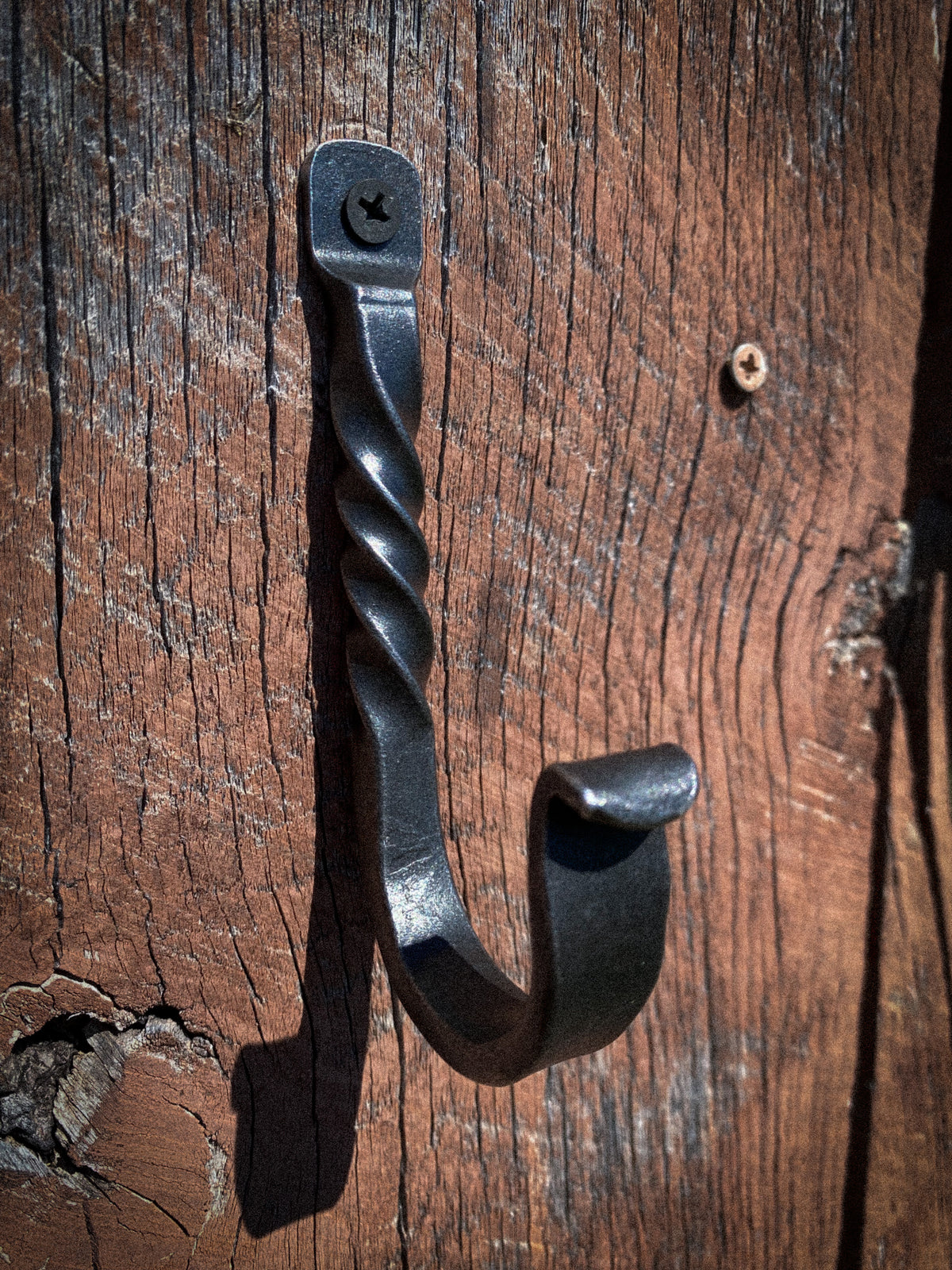 A rustic black metal hook with a twisted shaft and a curved hook end, mounted on a weathered brown wooden surface.