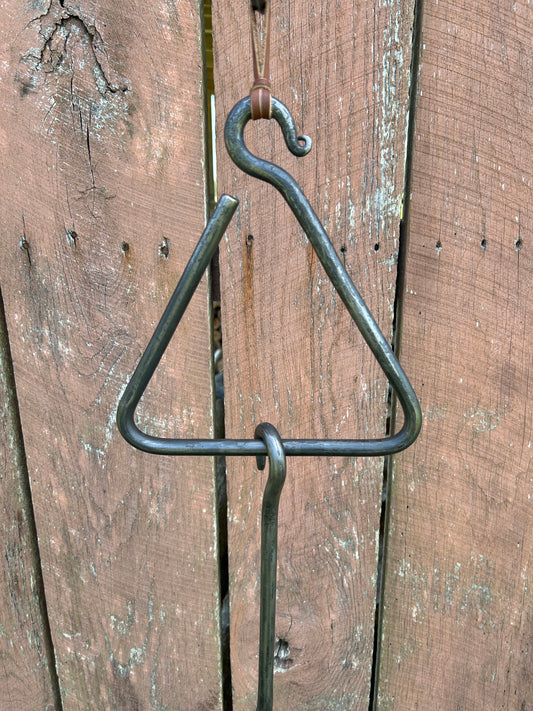 Hand-forged steel dinner triangle with leather hanging strap and striker on a rustic wood fence. Hutton Forge.

