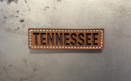 A rectangular brown leather magnet with the word TENNESSEE in dark brown letters, bordered by white stitching. Hutton Forge. 