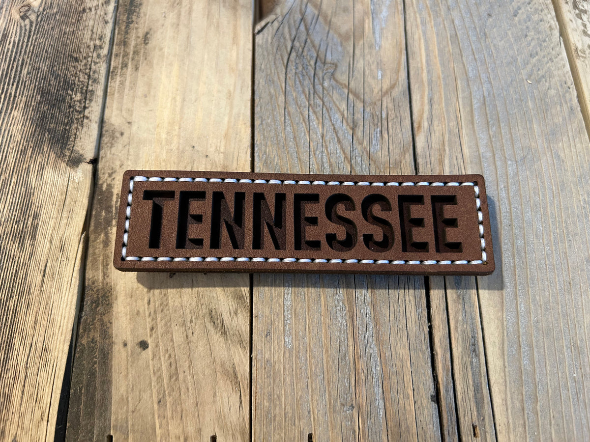 A rectangular brown leather magnet with the word TENNESSEE in dark brown letters, bordered by white stitching. Hutton Forge. 