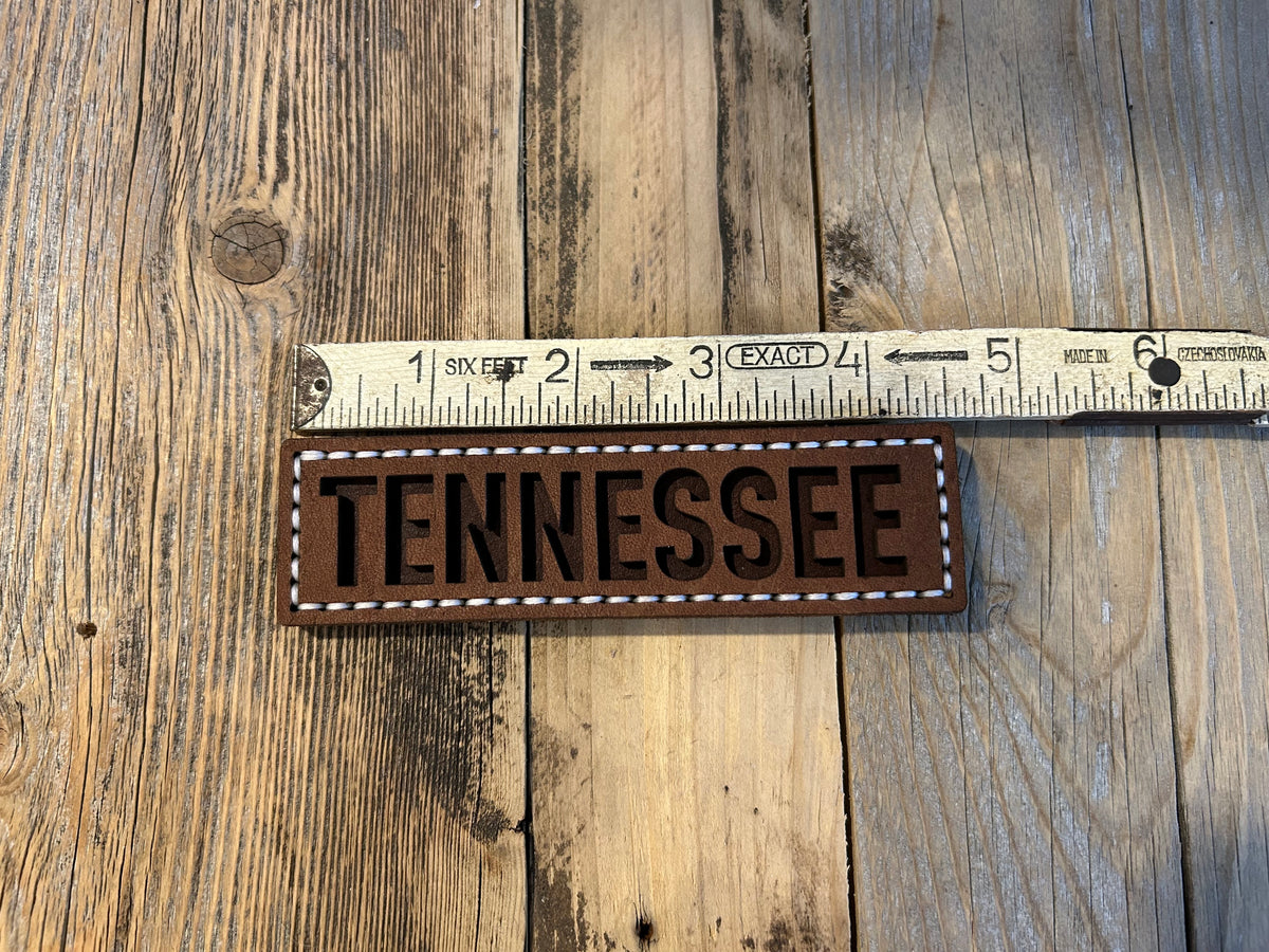 A rectangular brown leather magnet with the word TENNESSEE in dark brown letters, bordered by white stitching. Hutton Forge. 