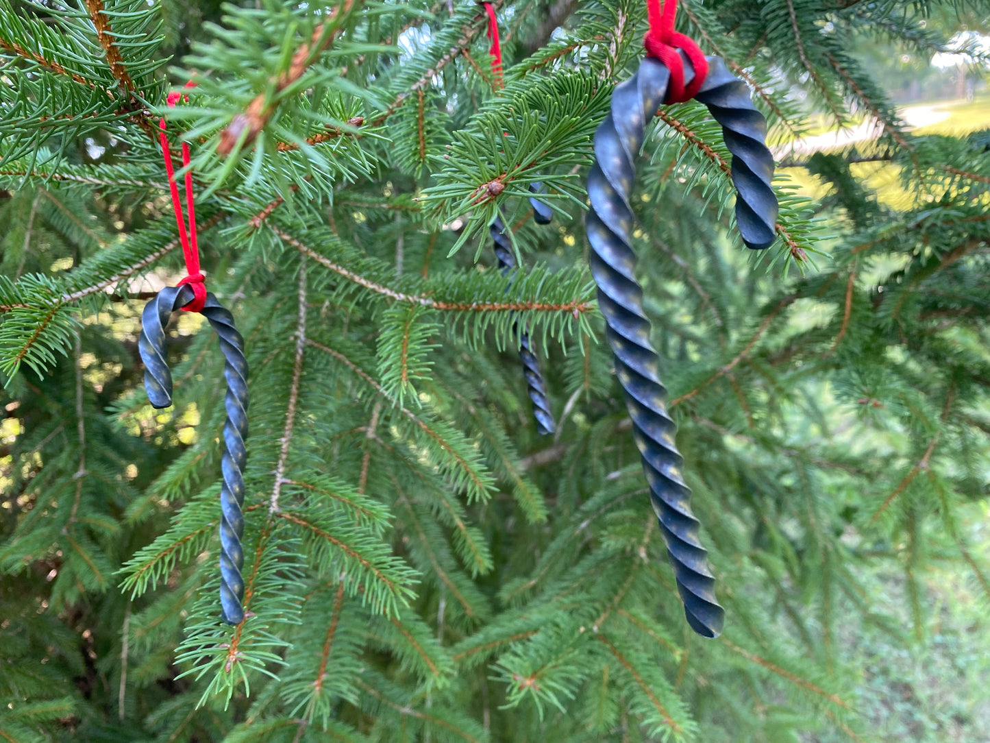 Hand Forged Twisted Steel Candy Cane Ornaments hanging from a red cord in a tree. Hutton Forge.