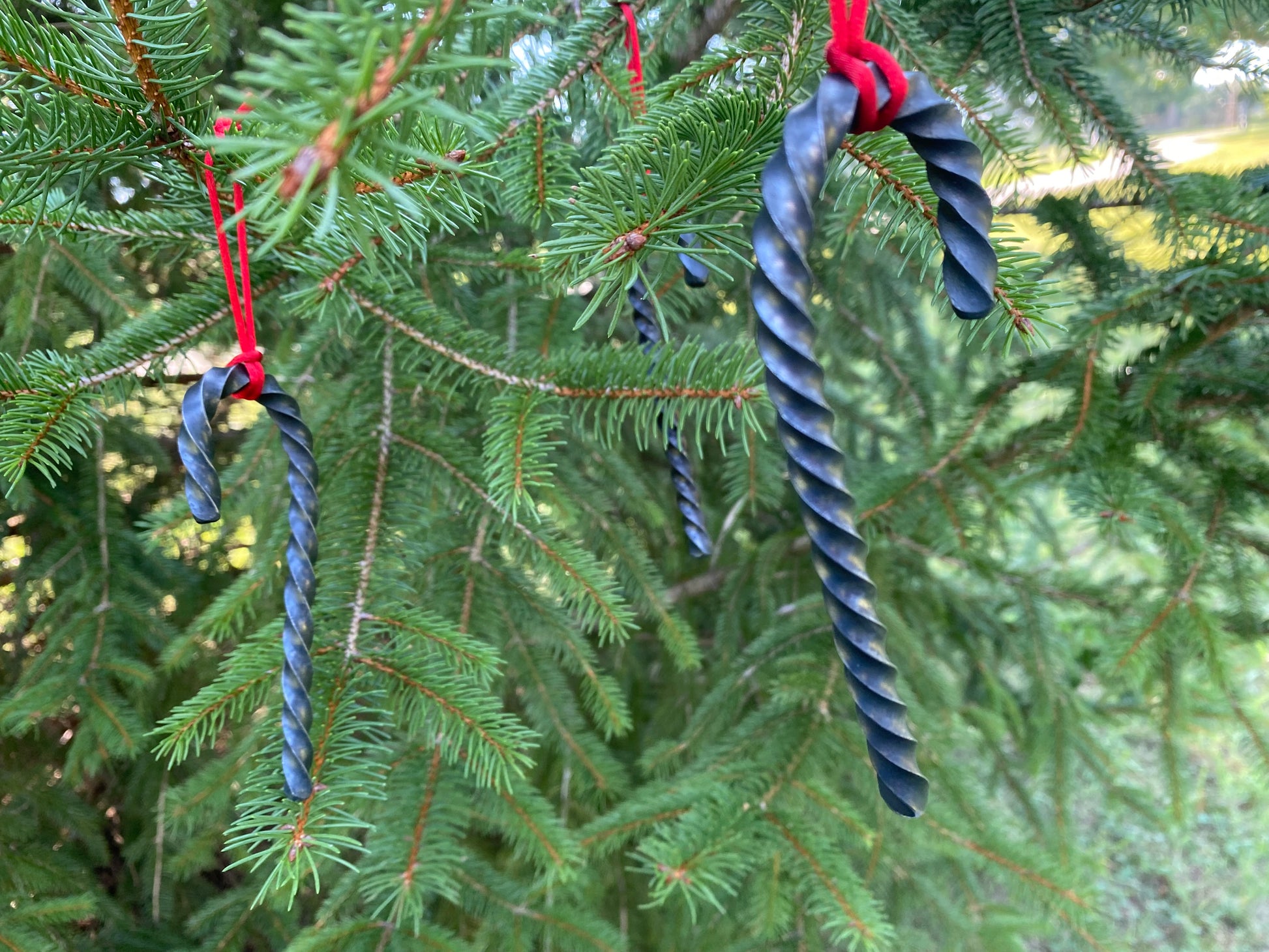 Hand Forged Twisted Steel Candy Cane Ornaments hanging from a red cord in a tree. Hutton Forge.