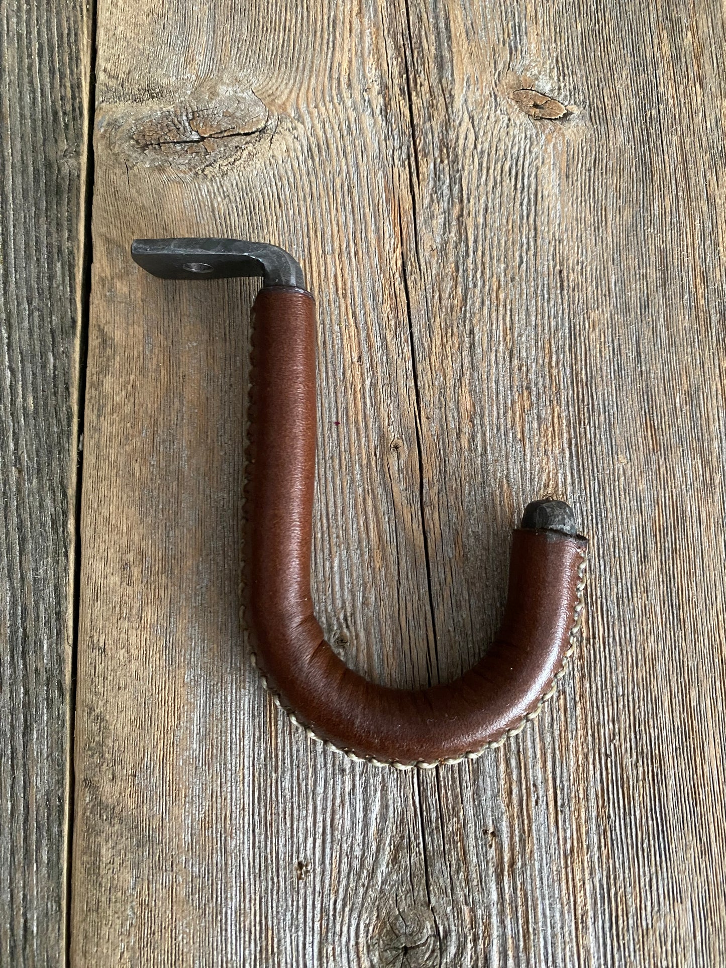 The steel hook has a padded leather section with white stitching. The hook is designed to be mounted under a cabinet or shelf to hang your mugs or other items.