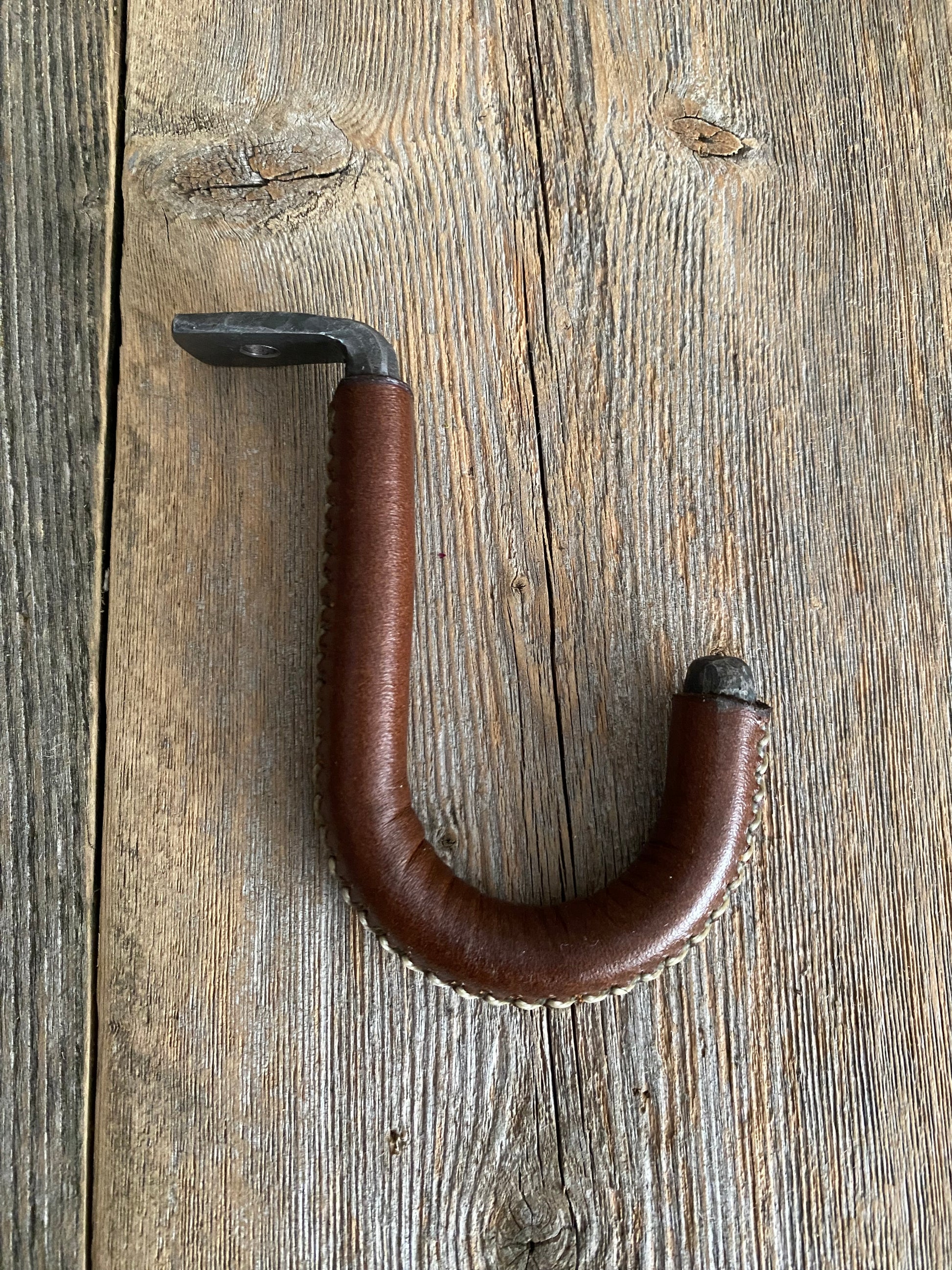 The steel hook has a padded leather section with white stitching. The hook is designed to be mounted under a cabinet or shelf to hang your mugs or other items.