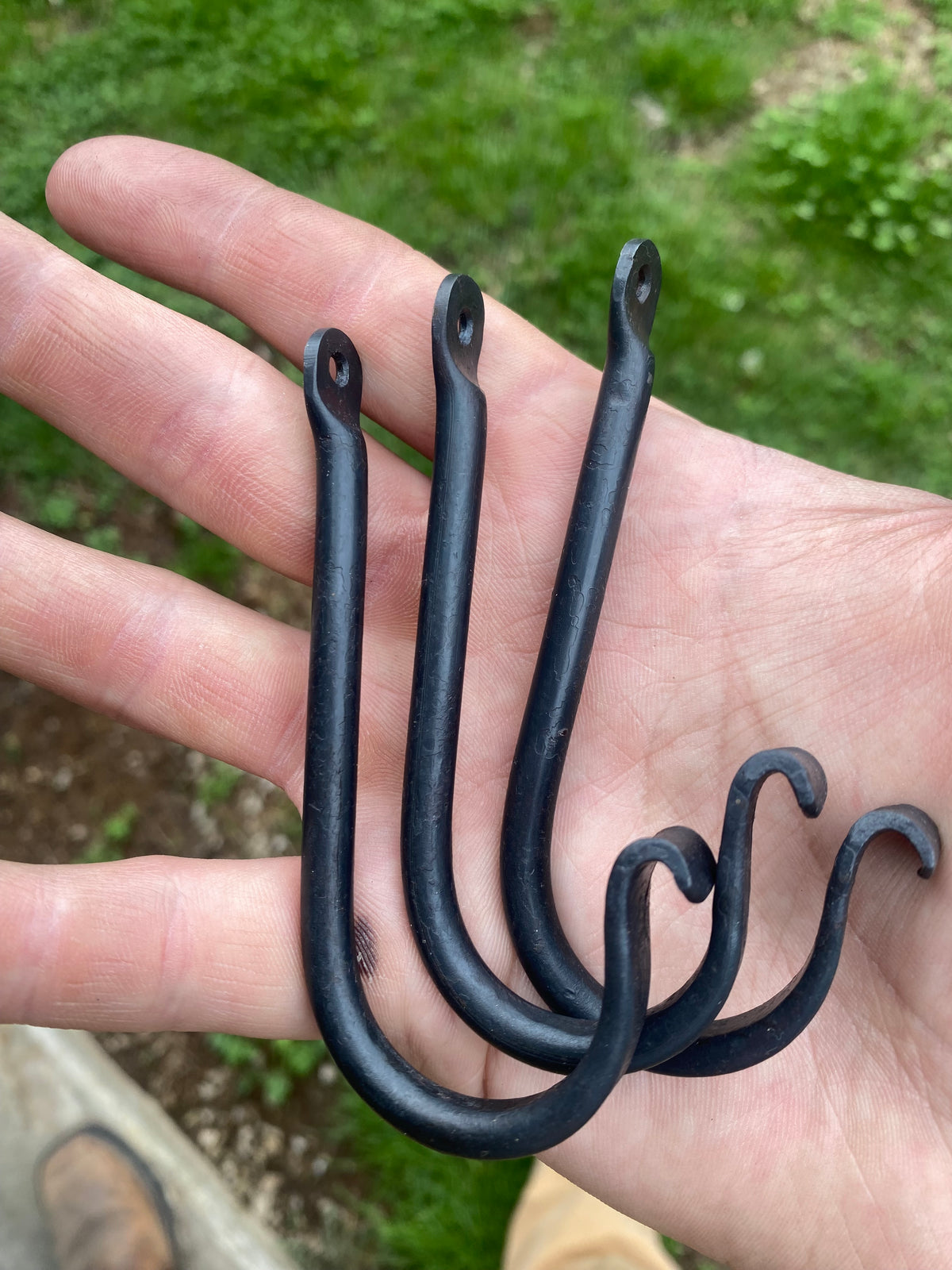  Hand-forged, black metal hooks with a curved design. The hooks feature a loop at the top for hanging and a curved bottom for holding items. 