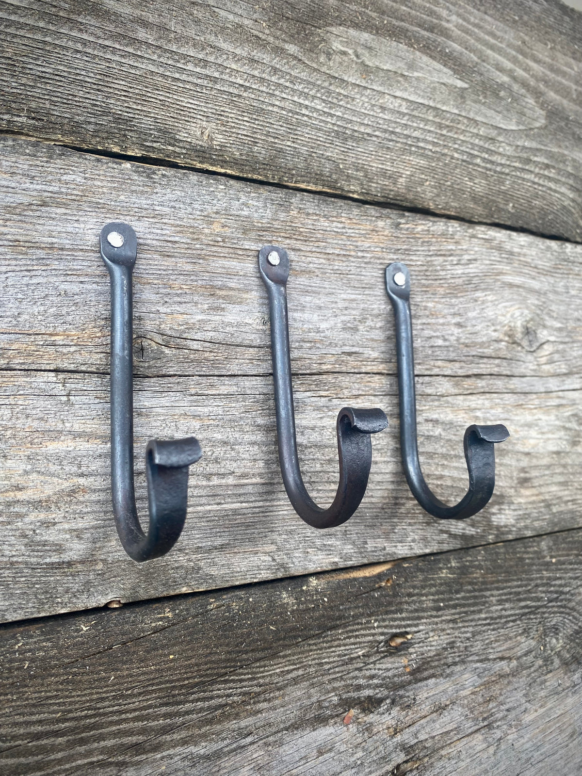 Set of three small rustic wall hooks, blacksmith-made from blackened steel, mounted on weathered wooden boards. Hutton Forge.