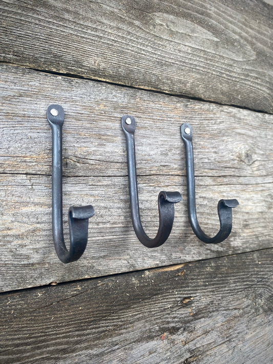 Set of three small rustic wall hooks, blacksmith-made from blackened steel, mounted on weathered wooden boards. Hutton Forge.