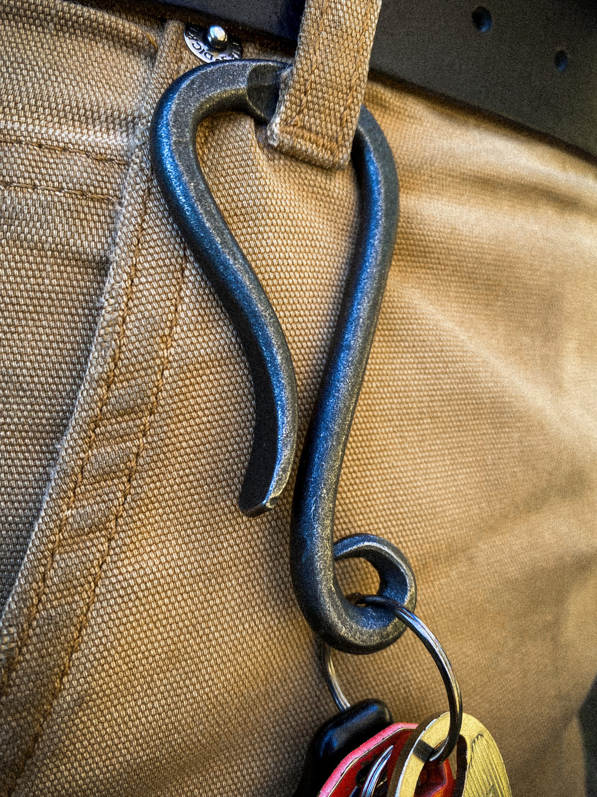 Hand-forged bottle opener keychain clipped to a belt loop, blacksmith made by Hutton Forge.