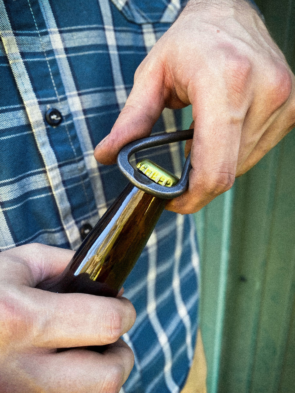 Hand-forged steel bottle opener keychain opening a bottle. Made by Hutton Forge.
