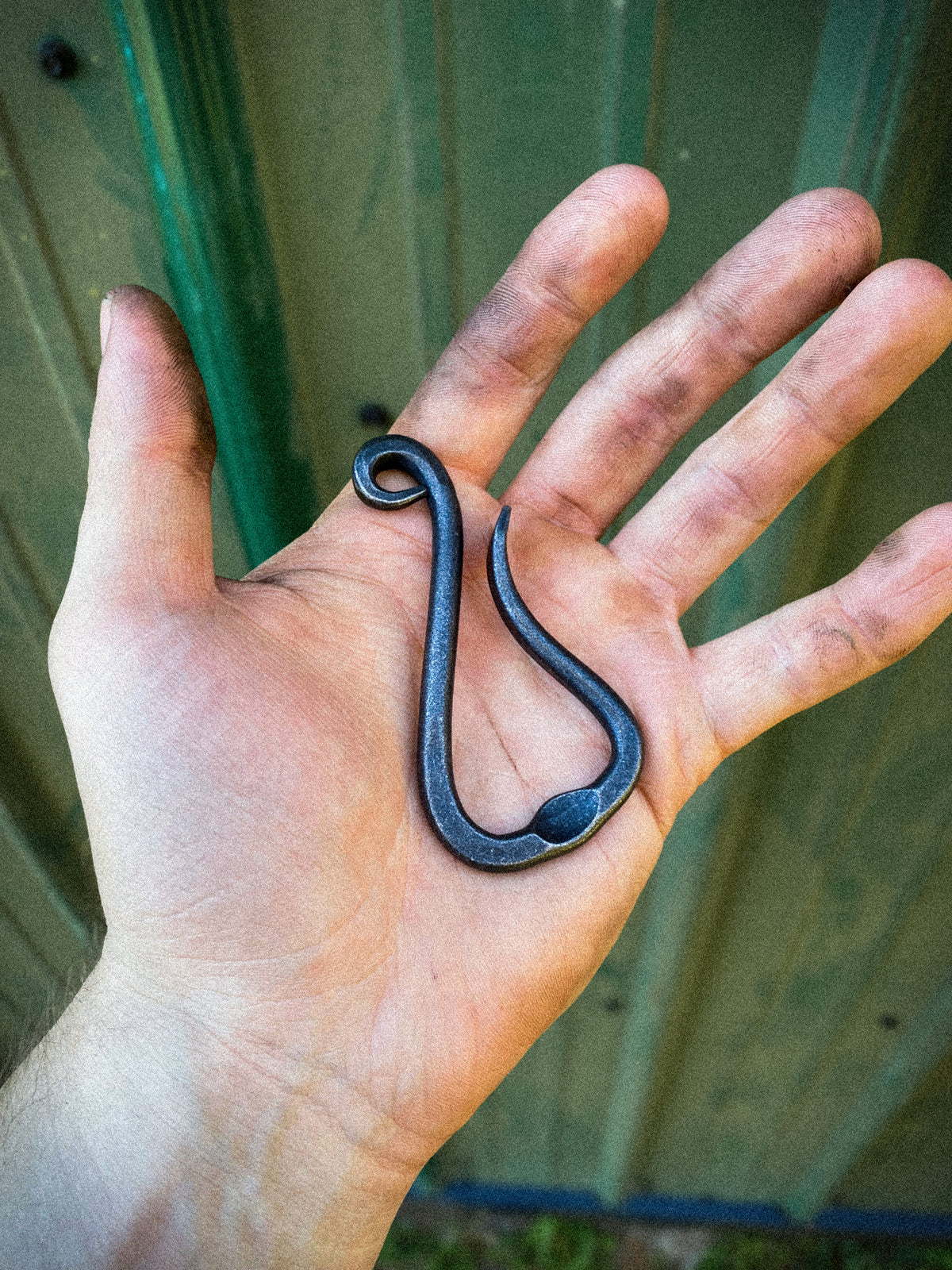 Hand-forged bottle opener keychain in the hands of the blacksmith. Made by Hutton Forge.