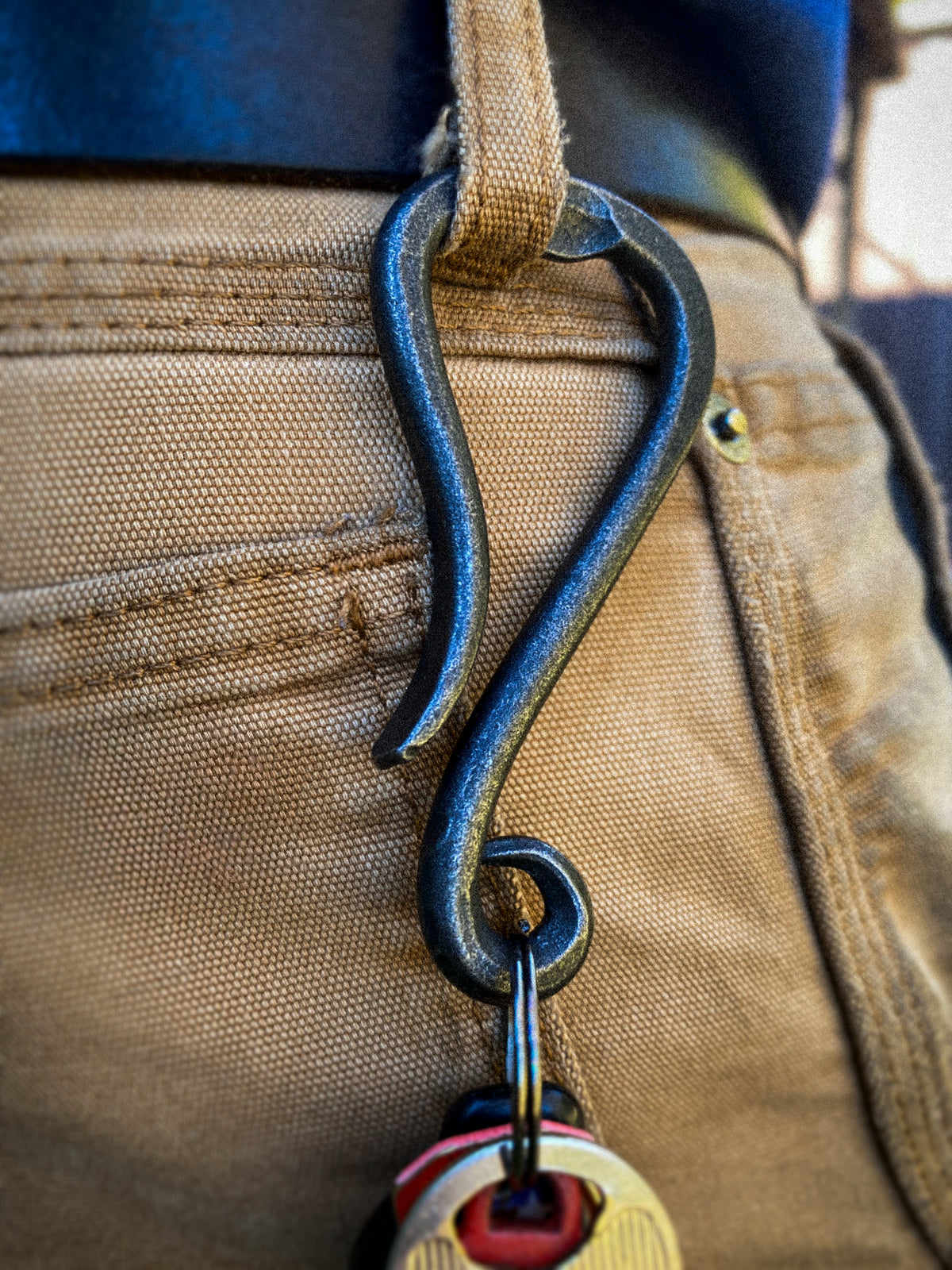 Hand-forged bottle opener keychain clipped to a belt loop, blacksmith made by Hutton Forge.