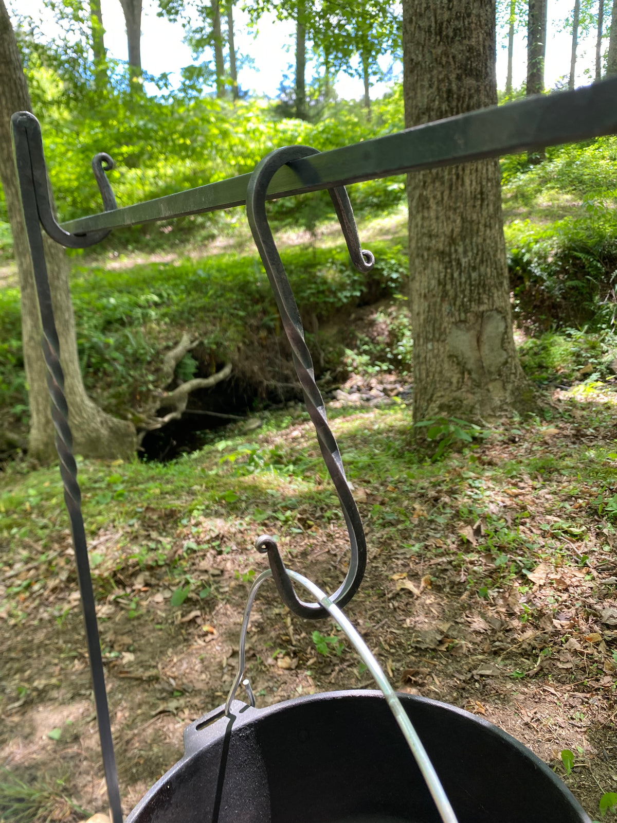  A handcrafted, dark metal campfire cooking set with an S-hook and a black cast iron pot. The hook can be used to hang the pot over a fire. Hutton Forge.