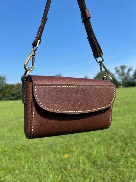 A brown leather crossbody bag with a flap closure and light contrast stitching, hand made by the Leathersmith at Hutton Forge. 