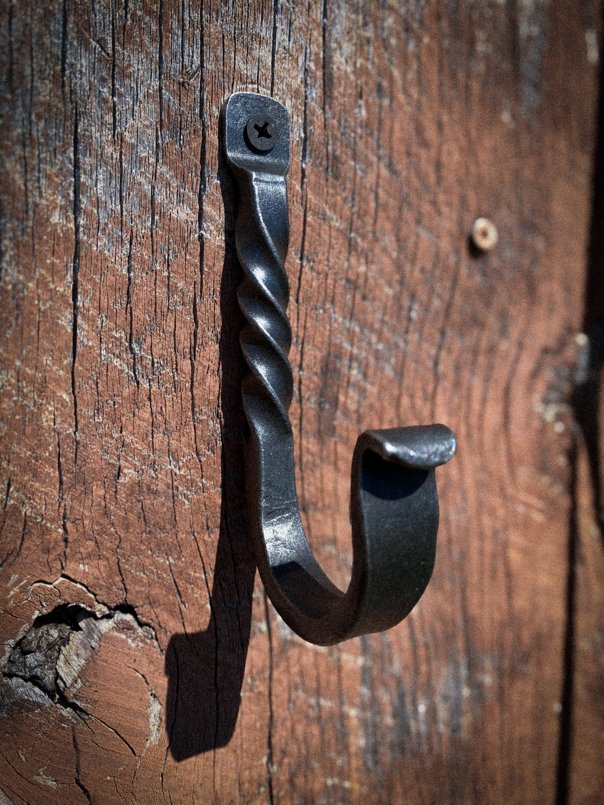 A rustic black wrought iron hook with a twisted spiral handle, mounted on a weathered brown wooden wall.