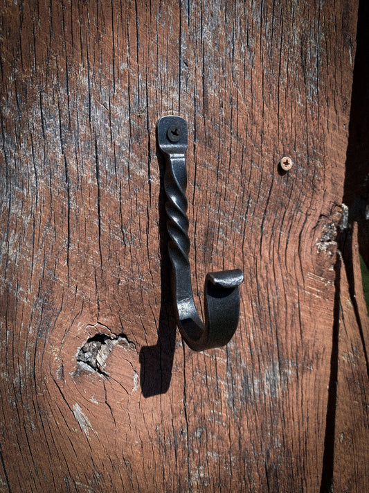 A black wrought iron hanging hook with a twisted shaft, mounted on a weathered brown wooden surface.