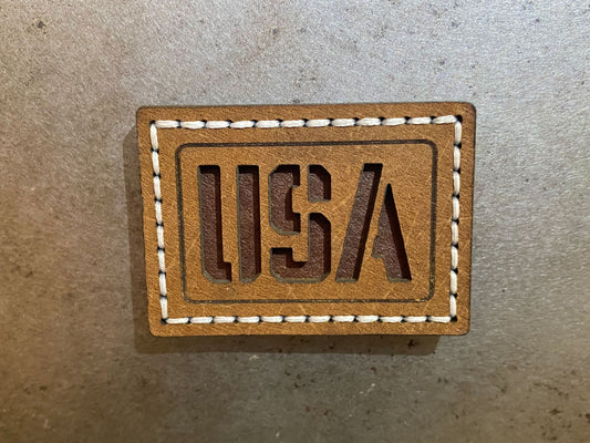 Hand-stitched brown leather magnet with cut-out “USA” lettering, white stitching on a rectangle design. Hutton Forge.
