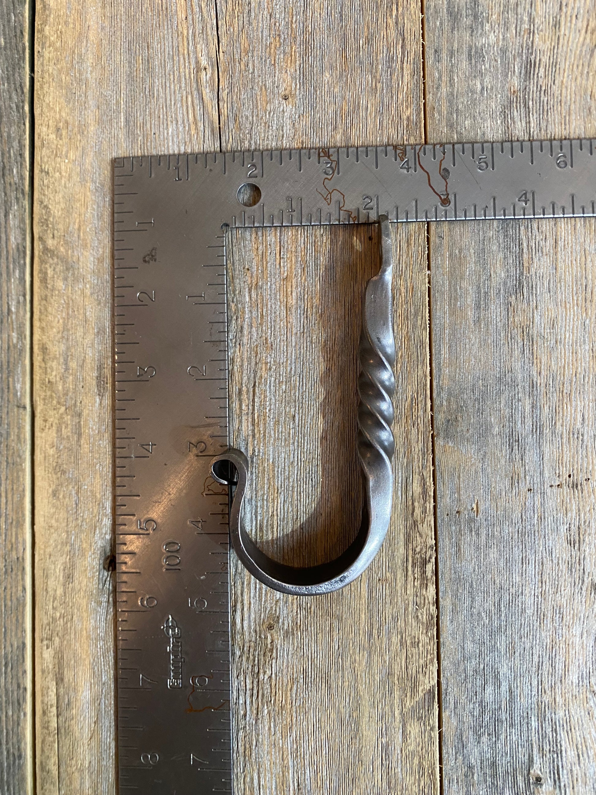 Metal j-hook on a wooden surface with a ruler for scale.
