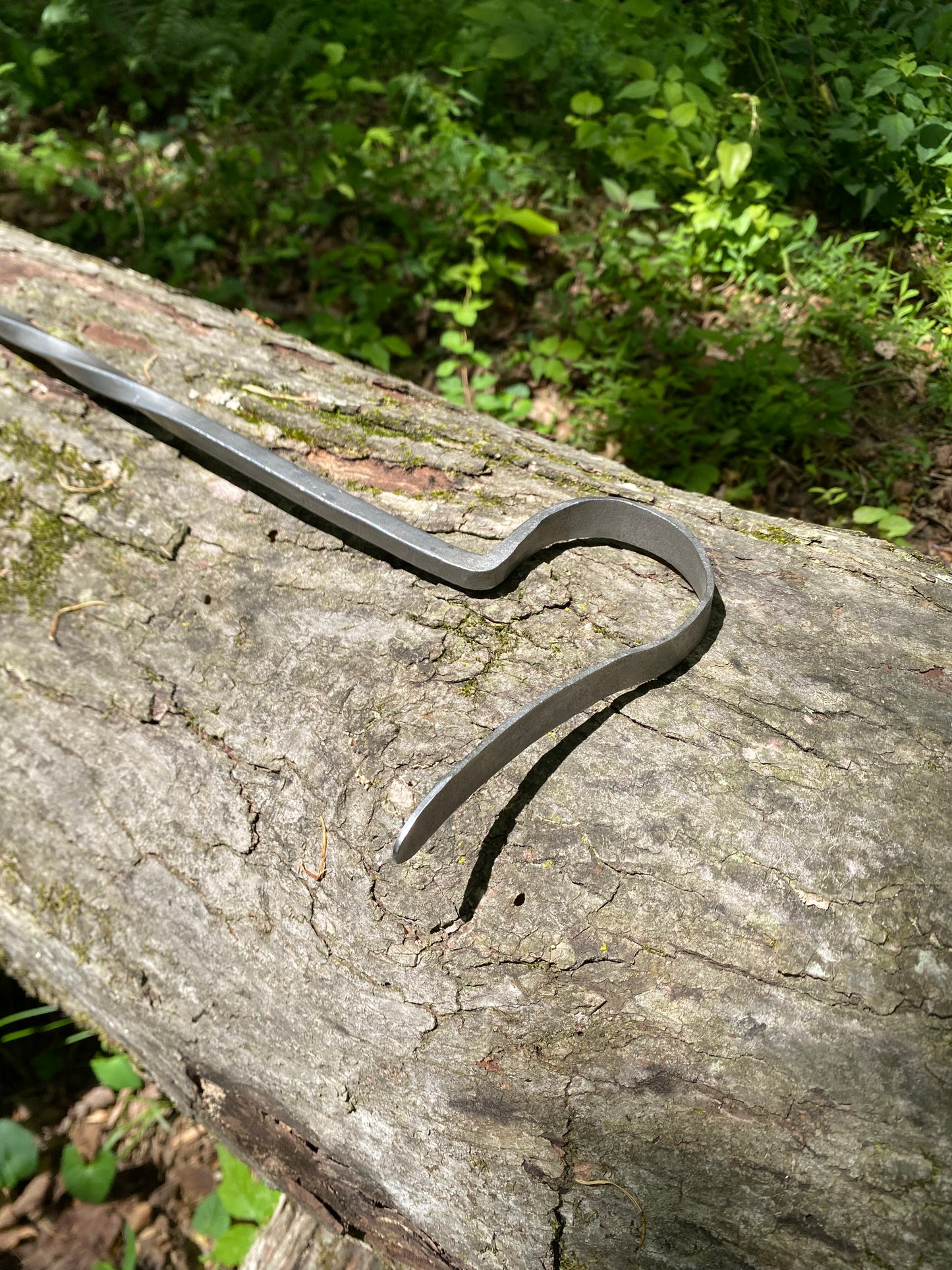 Handmade fire poker working end, resting on a textured tree log with a lush green forest background.