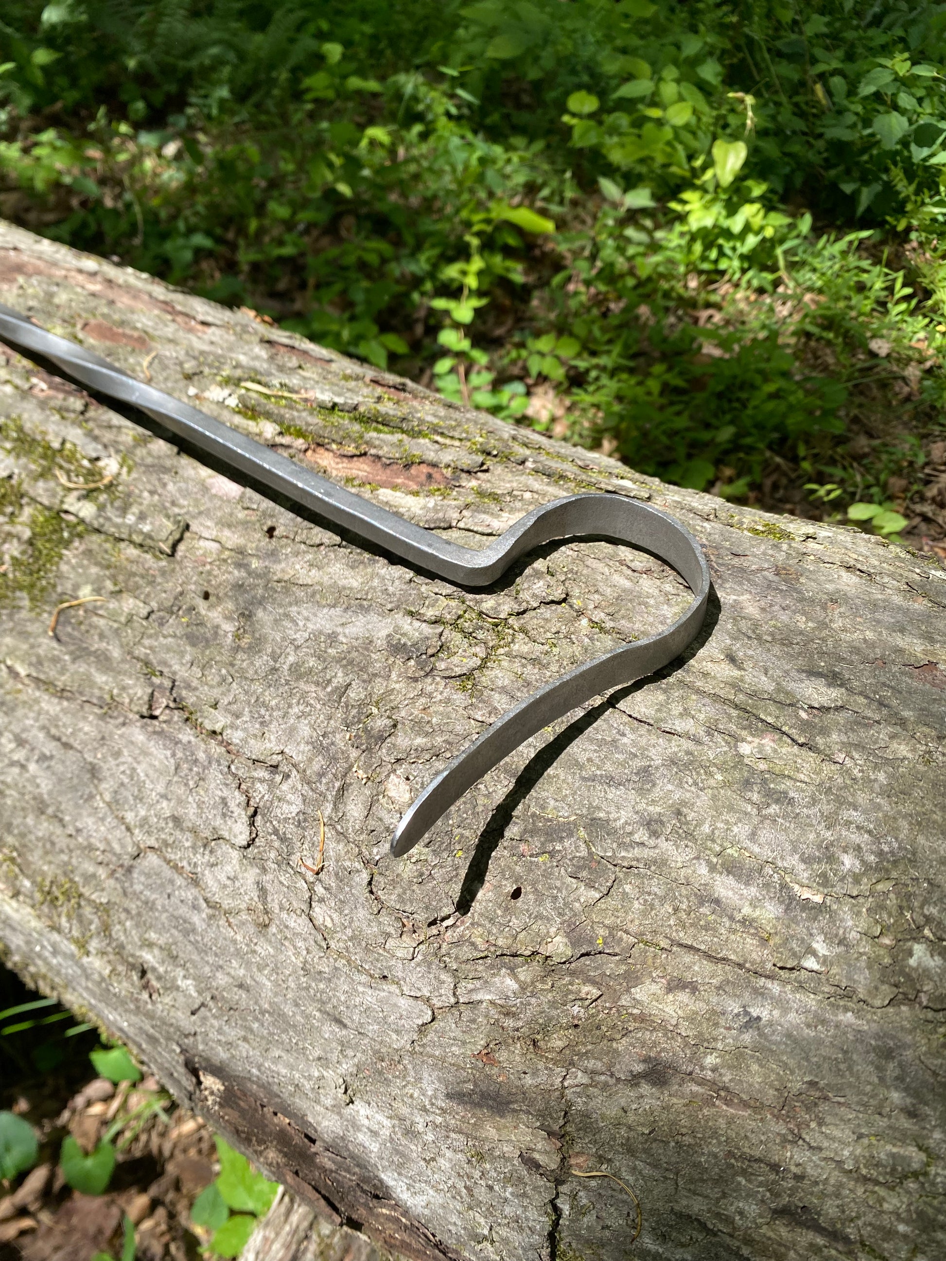 Handmade fire poker working end, resting on a textured tree log with a lush green forest background.