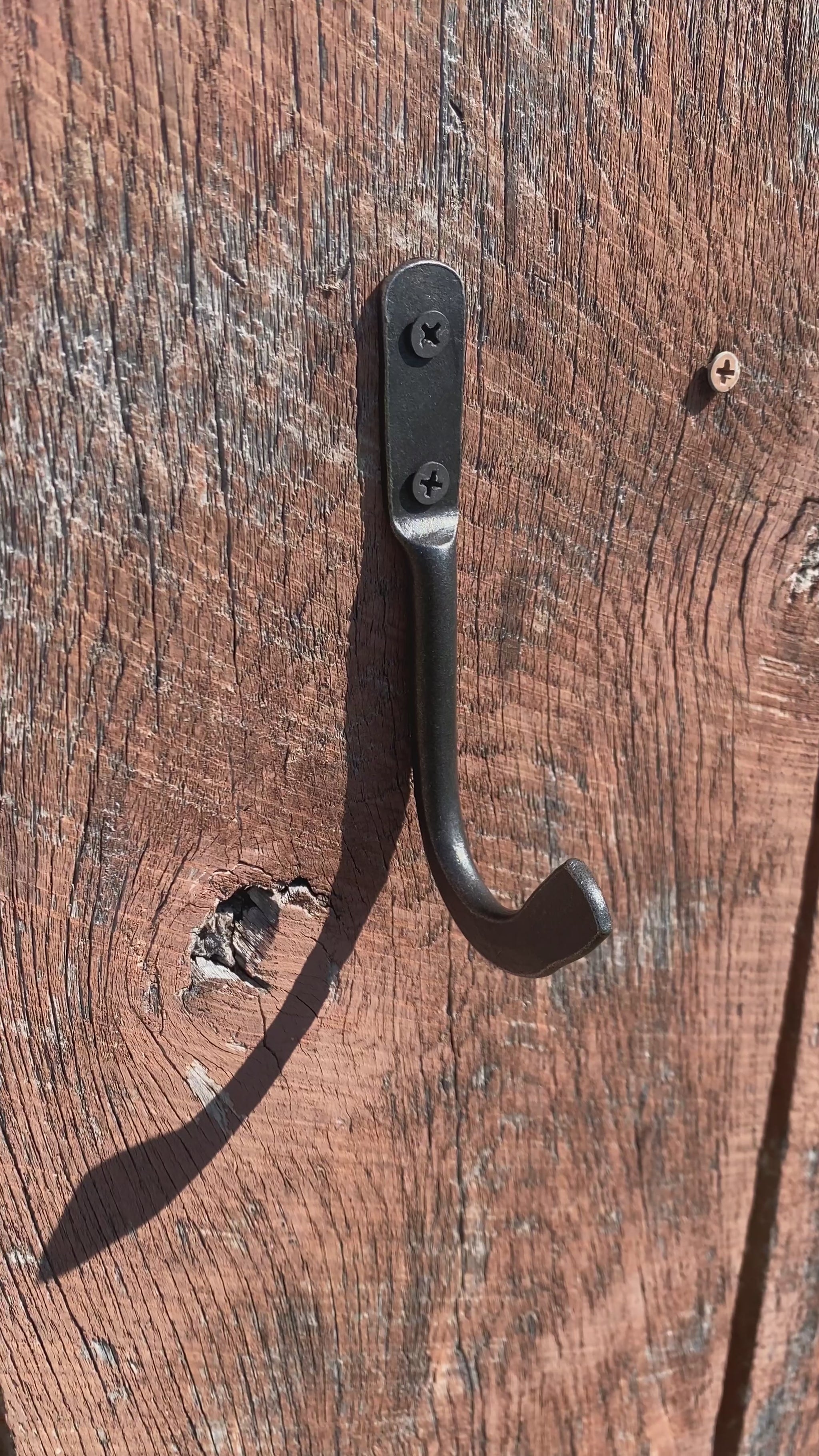 Hand-forged steel skillet hook holding a Lodge cast iron pan by the helper handle on a weathered wood wall. Hutton Forge.
