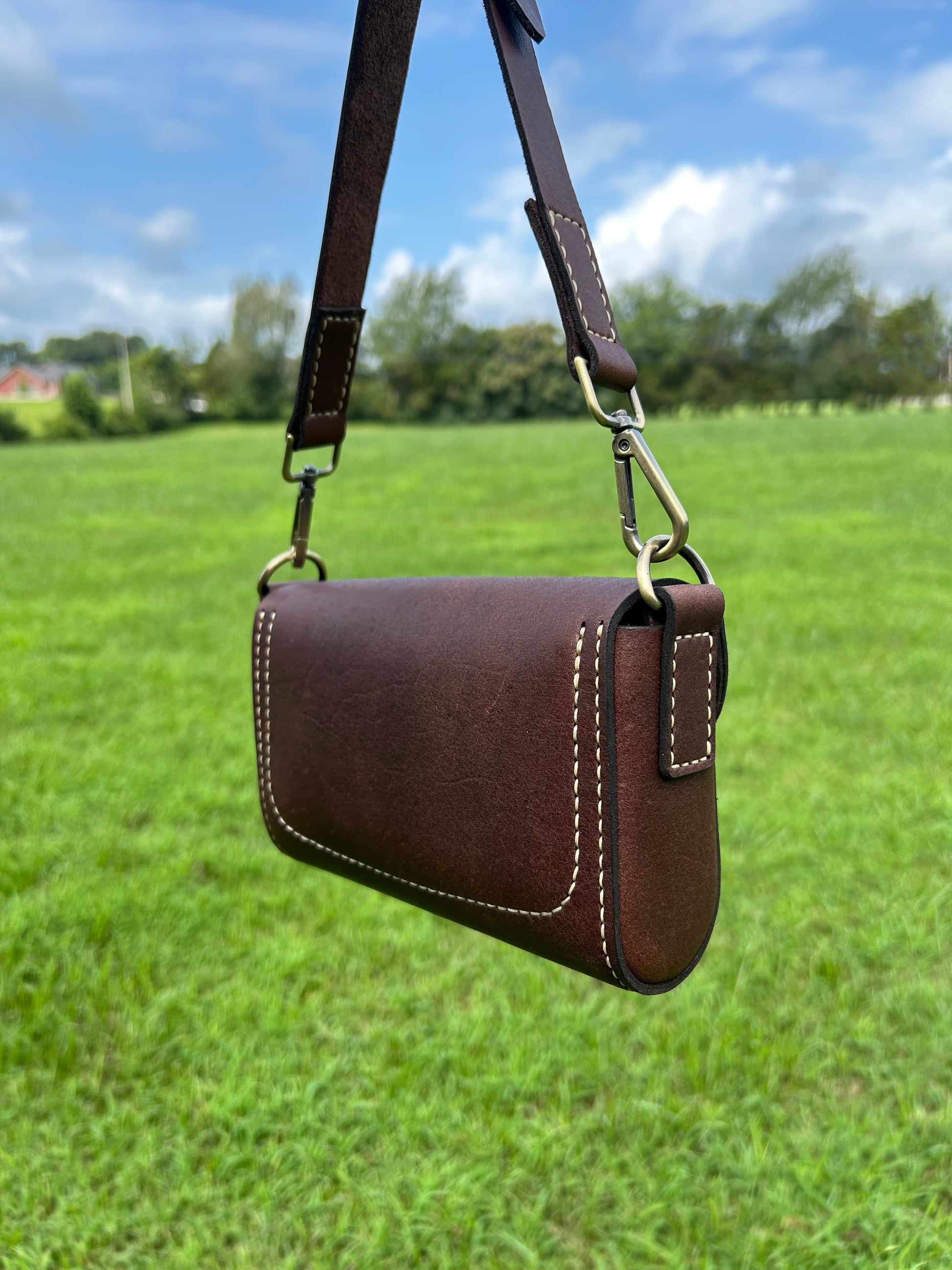 A dark brown leather crossbody purse with tan stitching and brass hardware, handmade by the leather smith at Hutton Forge.