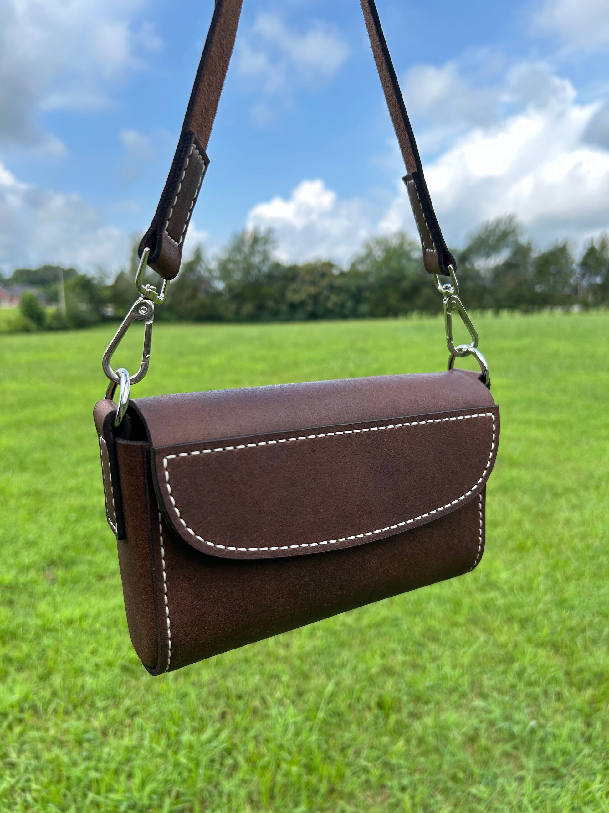 A dark brown leather shoulder bag with white stitching and silver hardware. Made by the leathersmith at Hutton Forge. 